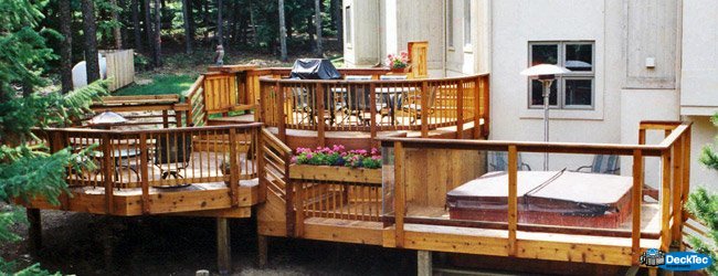 DeckTec custom designed grand deck with curved rails wood rails, glass paneling, flower boxes, fire place, and spa environment.