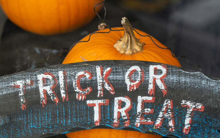 a trick or treat sign leaning against 2 pumpkins