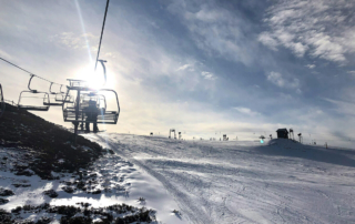 a ski lift chair with silhouettes and bright sun behind