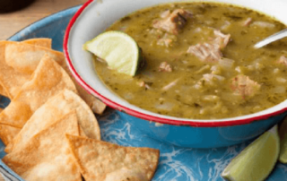 bowl of green chili with chips and a lime