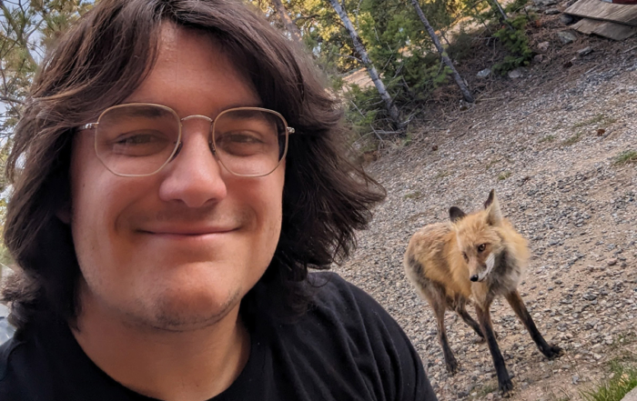 a guy smiling in the forest with a fox behind him